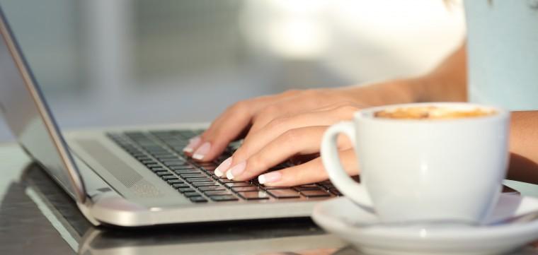 Close up of a woman hands typing in a laptop in a coffee shop terrace in the street